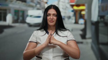 Kadın şehir sokaklarında güven içinde el kol hareketi yapıyor, günlük kıyafetlerini giyerken çeşitlilik ve vücut pozitifliği gösteriyor, kentsel çevre ile sorunsuz bir şekilde harmanlıyor..