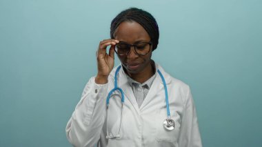 Gözlüklü ve steteskop takan kadın doktor mavi bir duvarın önünde duruyor, profesyonelliği aktarıyor ve sağlık hizmetlerine odaklanıyor..