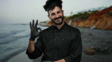 Siyah üniformalı İspanyol aşçı, kumsalda ve deniz dibinde eldivenleriyle güzel bir jest yapıyor. Gülümsüyor ve mükemmel bir aşçılık öneriyor..
