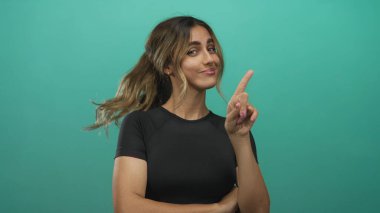 Genç sarışın kadın yeşil bir fotoğraf stüdyosunda parmağını yukarı kaldırarak işaret ediyor; güven oyunculuğu motivasyonu güçlendirme.