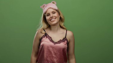 Pembe gece elbiseli bir kadın yeşil arka planda poz veriyor, neşe saçıyor ve enerjik titreşimler yayıyor, canlı ve eğlenceli bir atmosfer yaratıyor..