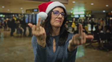Noel Baba şapkası ve gözlüğü takan orta yaşlı bir kadın havaalanı terminalinde yüzüklü orta parmağını gösteriyor..