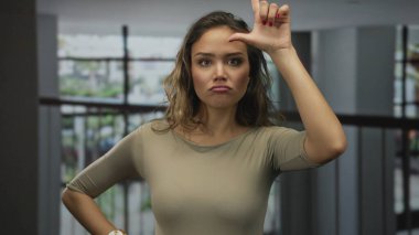 Genç İspanyol kadın modern ofis lobisinde alnına karşı ezik jestler yapıyor. Reddedildi..