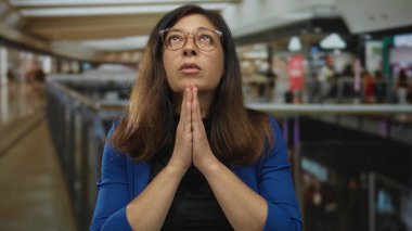 Alışveriş merkezinde el ele tutuşup dua eden mavi ceketli bir kadın. Umut..