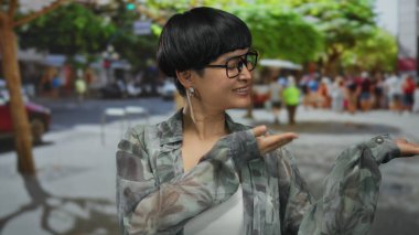 Kentsel sokak ortamında gülümseyen, el kol hareketi yapan şehir ışıkları altında neşeli bir ifade sergileyen, arabaların bulanık arka planı ve canlı metropoldeki yeşilliklerle çerçevelenmiş bir kadın..