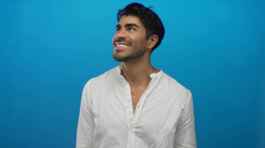 Mavi stüdyoda gülümseyen ve yukarı bakan bir adam çıplak boyun ve sakallı yumuşak ışık altında sakal; iyimserlik umut.