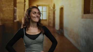 Yaşlı bir üniversite koridorunda gülümseyen genç bir kadın. Büyük pencerelerden içeri güneş ışığı giriyor. Sıcak ve sıcak bir atmosfer yaratıyor..