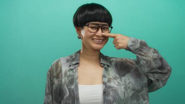 Gözlüklü genç Çinli kadın, yeşil bir arka plana bakarak mizah ve kendine güveni ifade ediyor..