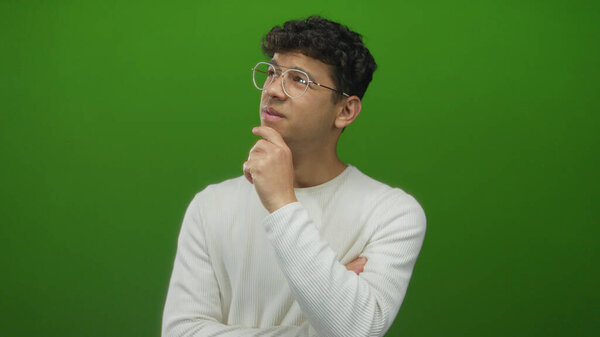 Человек с вьющимися волосами в очках и в белом свитере с рукой на подбородке в студии смотрит вверх; думая:.