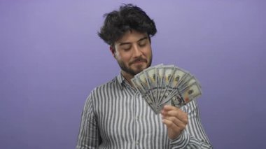 Sakallı genç adam, parlak bir mor arka plana karşı bize dolar tutuyor. Finansal bağlamda güven ve başarı yayıyor..