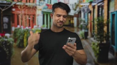 Canlı şehir caddesinde telefona kaşlarını çatmış genç İspanyol bir adam. Açık havada bulanık binalar, olası bir kafa karışıklığını ya da farkındalığı gösteriyor.