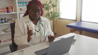 Doktor hastane odasında bir video görüşmesi yapıyor, elinde ilaç tutuyor ve bir hastayla meşgul oluyor, profesyonel bir tıbbi çalışma ortamı sergiliyor..