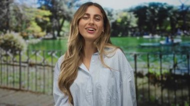 Gülümseyen sarışın kadın öpmek için dudaklarını büzüyor. Kamu parkında çitin kenarında öpüşmek için dudaklarını büzüyor..