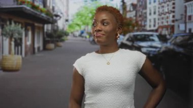 Genç Afrikalı Amerikalı kadın, park halindeki arabalarla ve tuğla bina cepheleriyle baş parmağıyla caddeyi işaret ediyor. Güveni güçlendiren cesaret..