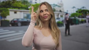 Sarışın kadın göz kırpıyor ve kameraya işaret ediyor yoğun sokak yaya geçidinde gün ışığında; şakacı flörtleşme.