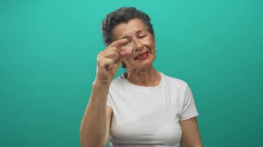 Küçük parmakları olan yaşlı bir kadın canlı yeşil arka plana gülümsüyor ve stüdyo ortamında neşeli bir ifade sergiliyor..