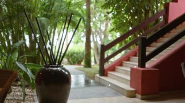 Lüks tatil köyü lobisinde ahşap çubuklu bulanık vazo ve dışarı çıkan zarif merdivenli tropikal yeşillik sakin ve davetkar bir atmosfer yaratıyor.