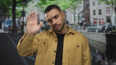 Sarı ceketli genç adam elini sallayarak caddede gözleri kapalı selam veriyor; sıcak karşılama.