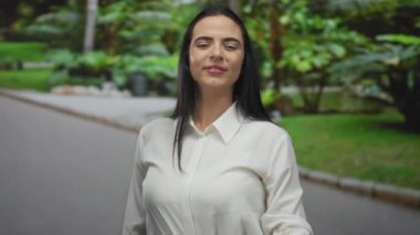 Beyaz gömlekli kadın yemyeşil bir parkta güçlü duygular ifade ediyor. Açık havada güçlü bir öfke ve kararlılık sergiliyor..