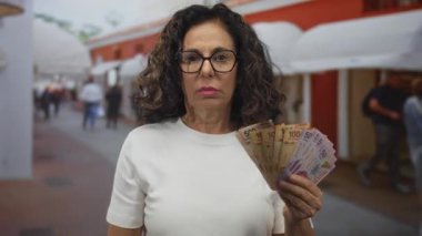 Orta yaşlı İspanyol kadın Meksika pezosu tutuyor. Açık havada heyecan dolu bir ortamda..