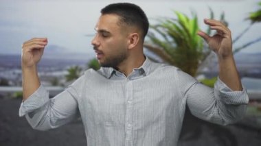 Genç İspanyol adam binanın önünde palmiye ağaçlarının önünde konuşuyor. Kolları kıvrılmış çizgili gömlek giyiyor. İletişim bağlantısı enerjisi coşkusu..