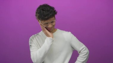 Gözlüklü ve süveter ören, rahatsızlık gösteren canlı mor stüdyoda yanakları ovuşturan bir adam..