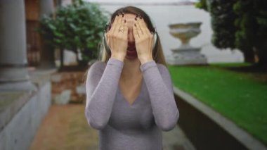 Dışarıda kulaklıklı bir kadın, neşeli bir şekilde yüzünü yemyeşil bahçeye kapatırken şaşırmış görünüyor. Heyecan ve neşe dolu duygular aktarıyor..