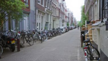 Amsterdam 'daki bulanık sokak manzarası, arka planda ve şehir yeşilliğinde klasik Hollanda mimarisi olan kaldırım taşı yolu boyunca dizilmiş bisikletleri yakalıyor..