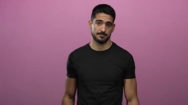 Genç, İspanyol asıllı bir adam, kollarını kavuşturmuş, kollarını kavuşturmuş, gündelik siyah giysiler giymiş, modern tarz ve cazibesini sergiliyor..