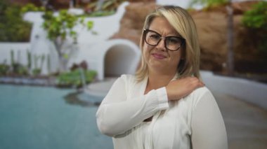 Beyaz bluz giyen, omuz omuza gezen ve havuz kenarında kaşları çatık bir kadın..