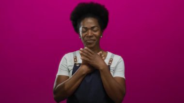 Önlük giymiş, elleri göğsünde pembe arka planda gülümseyen, sıcaklığını ve neşesini ifade eden, izole edilmiş ve güzel bir şekilde yakalanmış bir kadın..