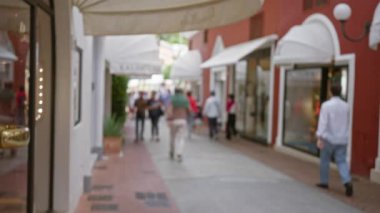 Pahalı Capri caddesinde güneşli bir gökyüzünün altında bulanık vitrinler ve güneşli tentelerle yürüyen insanların odaksız görüntüsü..