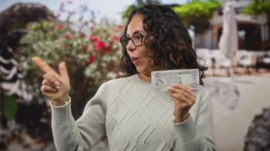 Dışarıda gülümseyen bir kadın elinde Dirham banknotuyla heyecanla bir şehir caddesini işaret ediyor..