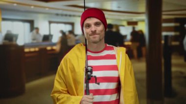 Çizgili gömlekli ve sarı ceketli mutlu bir adam otel lobisinde duruyor, rahat bir şekilde gülümsüyor, ev içi temalı eşsiz bir ortam yakalıyor..