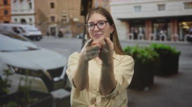 Yoğun şehir caddesinde park etmiş kamyoneti olan kamerayı işaret eden gözlüklü bir kadın..