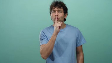 Yeşil arka planı olan, mavi gömlekli, sessiz ve gizlilik vurgulayan bir adam..