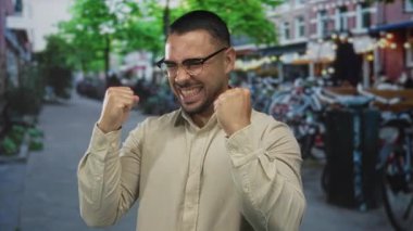 Latin kökenli genç adam sokakta yumruklarını sıkar ve gülümser. Zafer heyecanını kutlar..