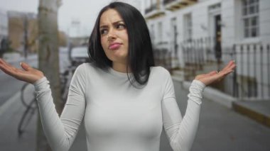 Şehir sokaklarında kafası karışmış bir kadın, beyaz bir tişört giyiyor, şehir zeminine karşı sorguluyor, kalabalık bir sokakta kargaşa yaratıyor..