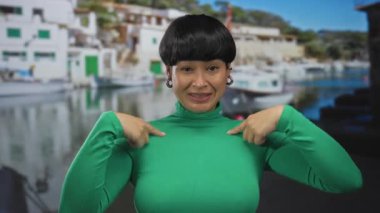Yeşil süveter giyen, arka planda tekneler ve binalar olan bir kadın açık hava eğlence sahnesinde kadın portresi olan bir süveter giyiyor..
