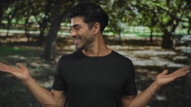 Adam uzun meşe ağaçları arasında açık yeşil orman parkında kollarını kaldırmış avuçlarını gösteriyor. Mutluluk..