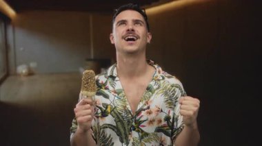 Genç adam tropikal bir tişört giyip otelde dondurma yemekten hoşlanıyor..