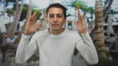 Açık havada gülümseyen genç İspanyol adam. Etrafı yemyeşil palmiye ağaçları ve tropikal gökyüzü altında boş zamanların tadını çıkarıyor..