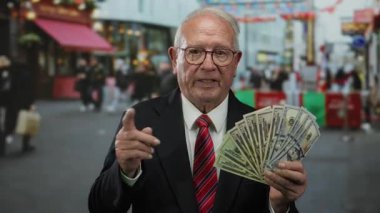 Kıdemli adam, renkli dükkanlar ve hareketli atmosferli şehir ortamında zenginlik ve iş başarısını ifade eden hareketli caddelerde bize dolar tutuyor.