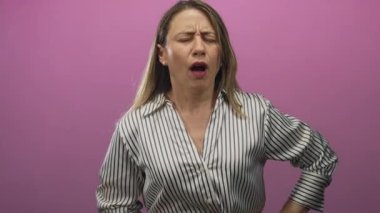 Sarışın kadın belini tutuyor ve pembe arka planlı renkli stüdyo çekimlerinde yüzünü buruşturuyor..