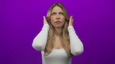 Kadın kulaklarını elleriyle kapatıyor, başını yukarı eğiyor ve bir fotoğraf stüdyosunda gözle görülür bir şekilde kaşlarını çatıyor; stres, sinir bozucu, sinir bozucu, sinir bozucu ve sinir bozucu..