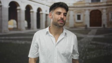 Adam, tarihi taştan kadim kemerler ve yıpranmış kaldırımlarla kaplı güneş ışığı altındaki tarihi caddede kamerayı işaret ediyor..