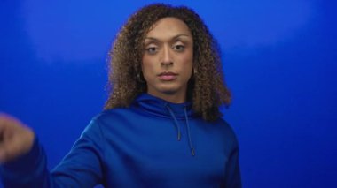 Mavi bir stüdyoda transseksüel İspanyol bir kadın eli kapüşonlu ve yüzünde odaklanmış bir ifadeyle iyi bir işaret yapıyor..