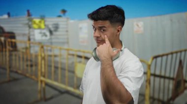 Şehir caddesinde inşaat alanında duran kulaklık takan genç bir adam..