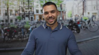 Mavi polo tişört giyen genç İspanyol adam gülümseyip ellerini caddeye park ederek açıyor; dostça bir coşku..