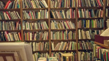 Görünür ahşap raflar ve kapalı odak bokeh etkisi ile bulanık bir kütüphanede renkli kitaplarla dolu kitaplıklar..